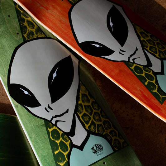 Two skateboard decks with alien graphics on a wooden surface