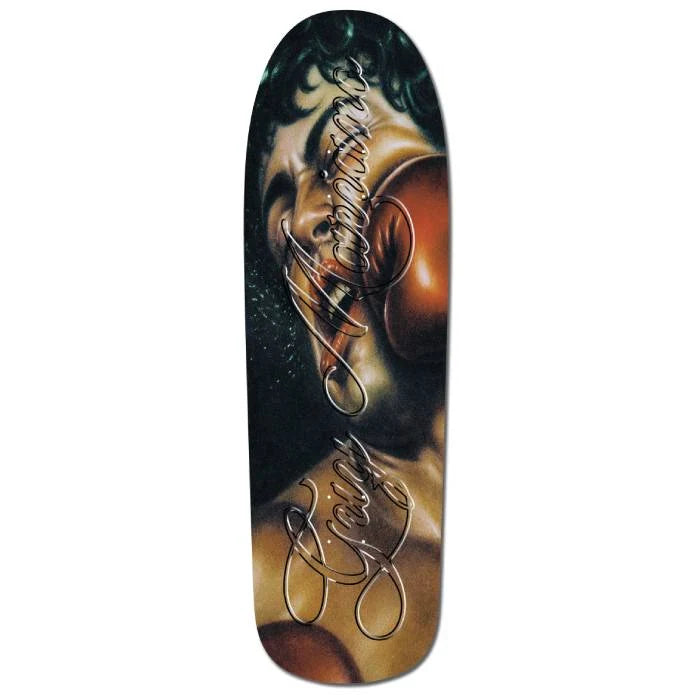 A skateboard deck featuring a stylized graphic print of a woman's face in warm brown and gold tones with dark green hair, overlaid with metallic silver script signatures.