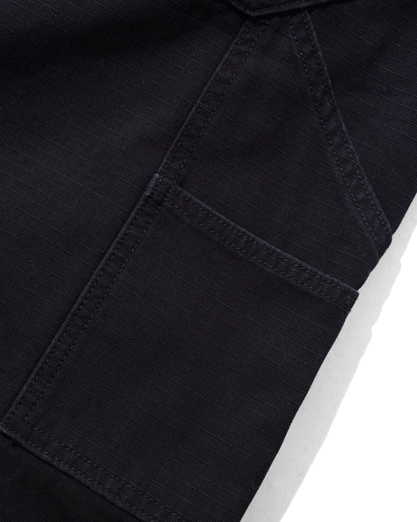 Close-up detail of a black denim garment showing a pocket seam and fabric texture against a white background.