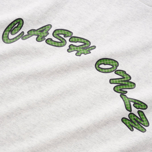 Close-up of a white heather t-shirt featuring a green plaid patterned script graphic that reads 'cash only' with a black outline.