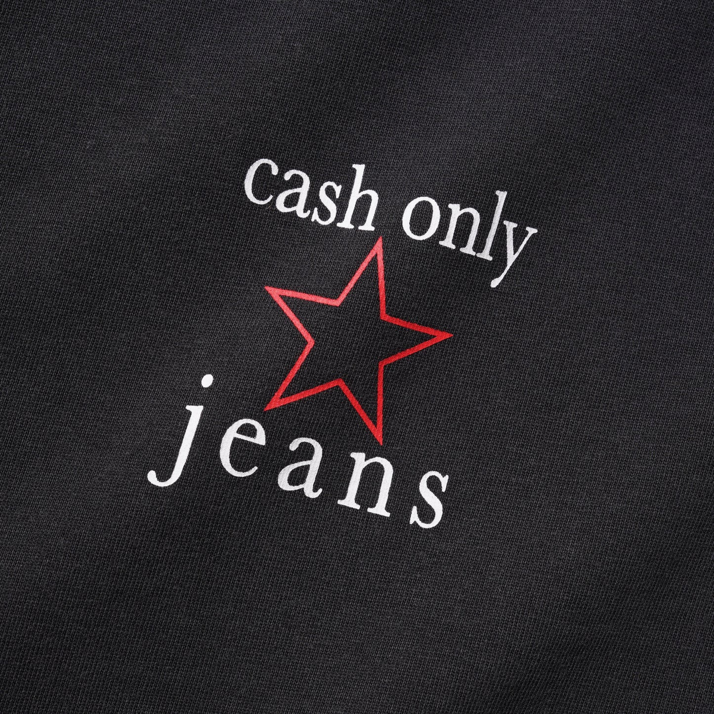 Close-up of a black fabric surface with white text reading 'cash only jeans' and a red outlined star graphic between the words.