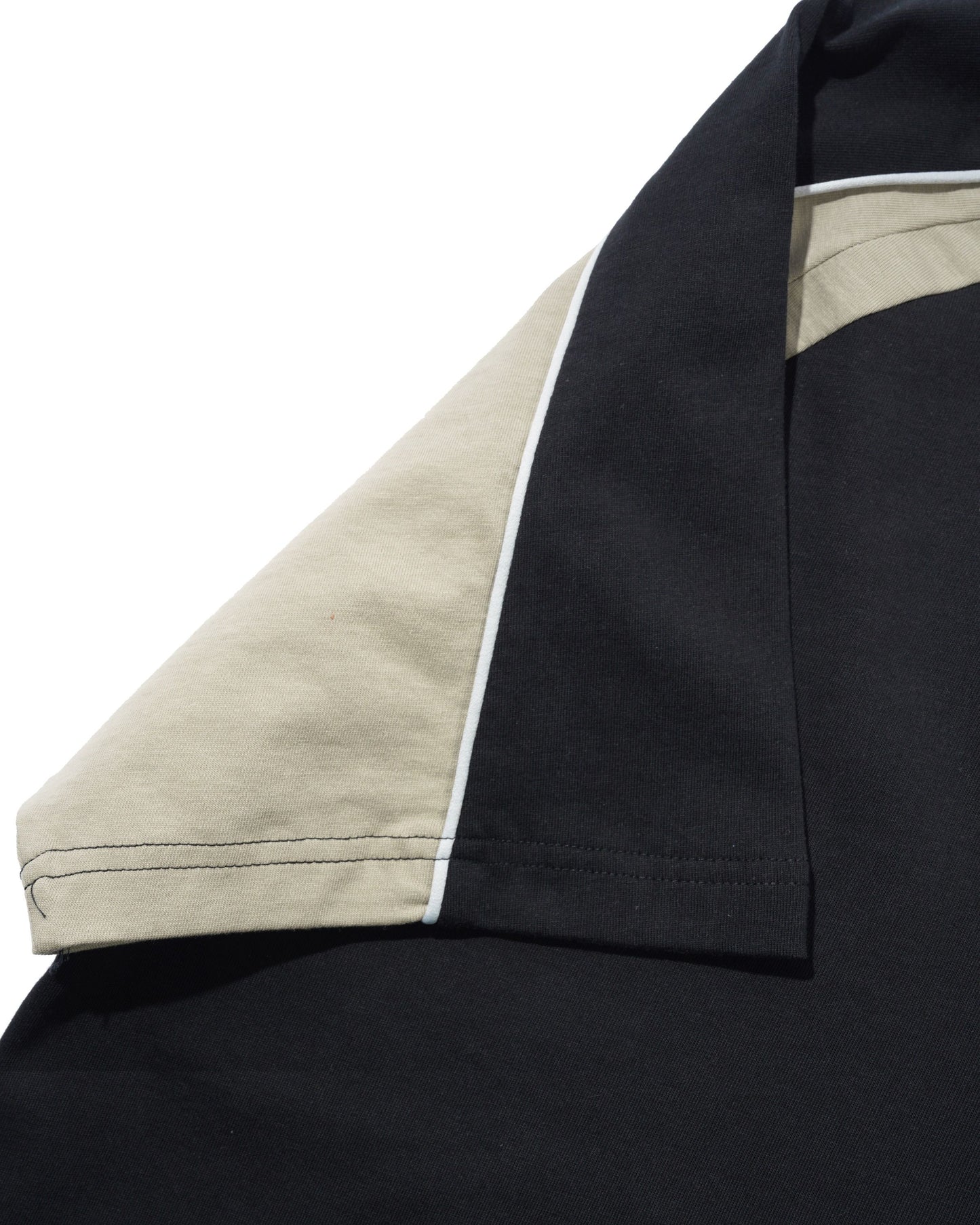 Close-up of a black short-sleeve shirt with a contrasting light beige inner sleeve and a thin white piping detail along the sleeve edge.