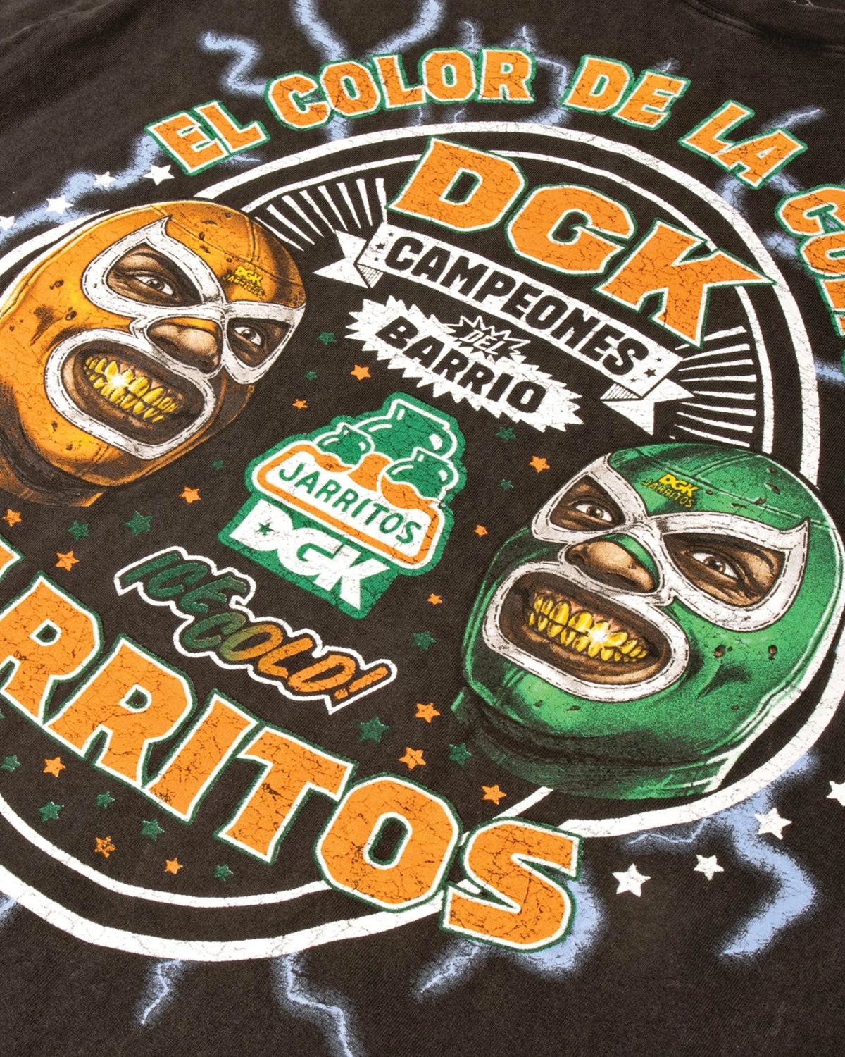 Close-up of a black graphic t-shirt featuring two Mexican wrestling masks, one orange and one green,