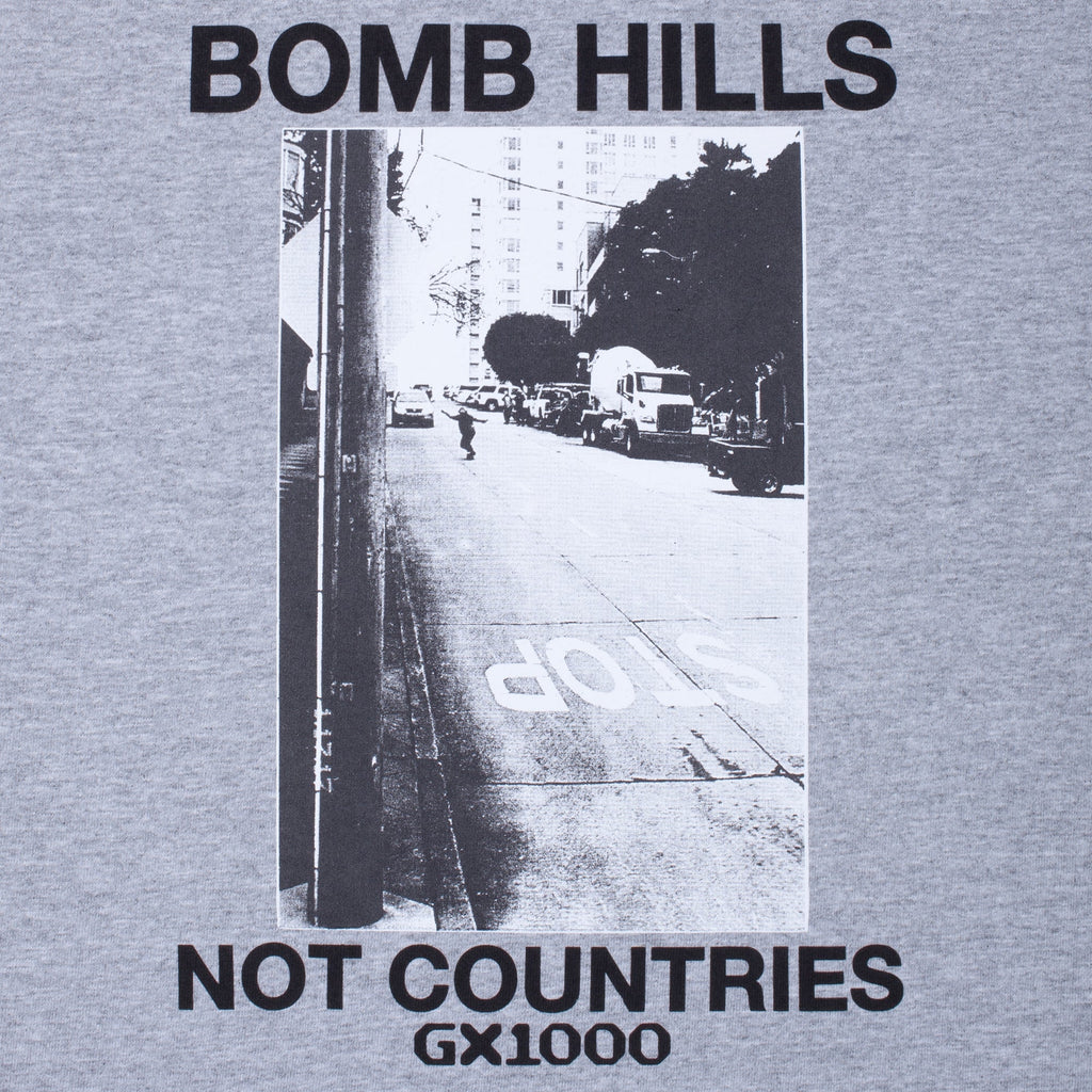 Gray t-shirt with black and white street scene and text 'BOMB HILLS NOT COUNTRIES GX1000' on a gray background