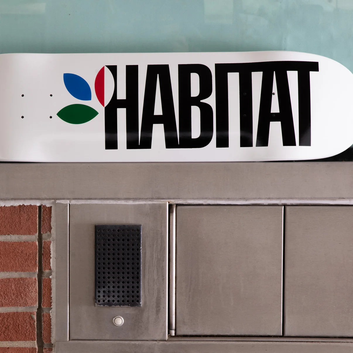 A white Habitat-branded sign or panel mounted above a metal mail slot and brick wall.