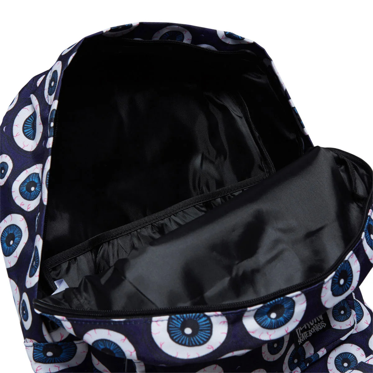 A close-up of a backpack's open interior showing a black nylon lining, with the exterior pattern visible on the left and right sides. The backpack features a dark navy blue base with a repeating pattern of white and blue circular eyes with small pink highlights.