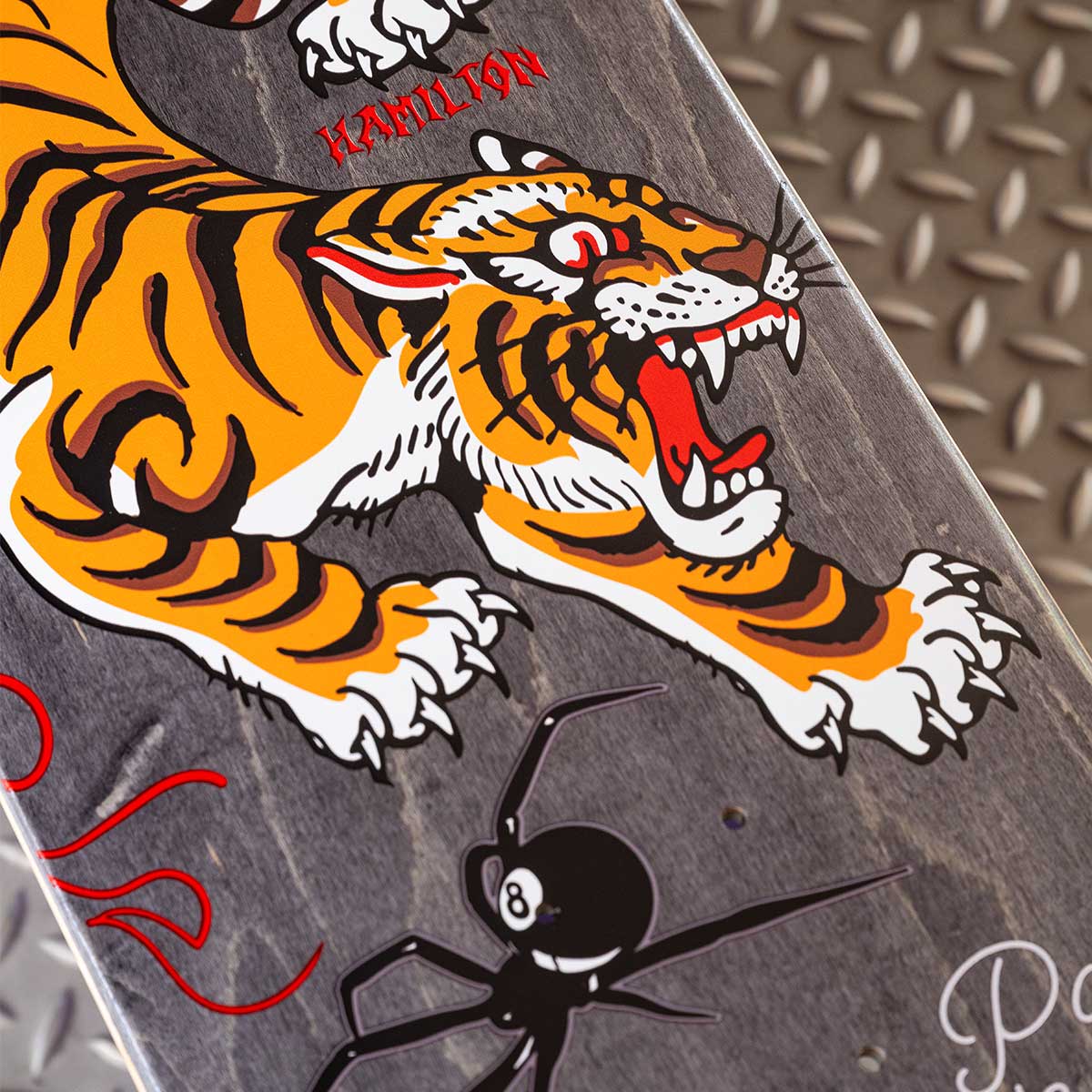 Skateboard deck with a tiger and spider design on a metallic surface