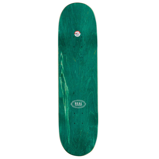A green skateboard deck with a natural wood grain pattern, featuring a white oval 'REAL' brand logo in the center and a small sticker near the nose, shown against a plain white background.