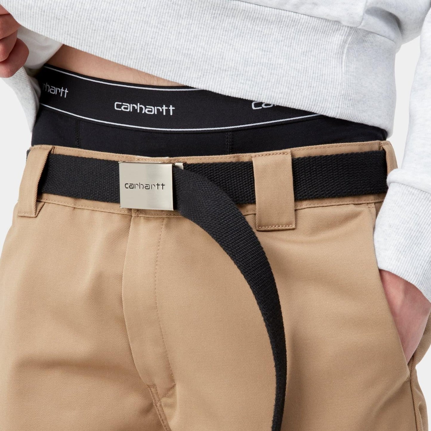 Person wearing beige pants with a black belt and white shirt, featuring Carhartt branding.