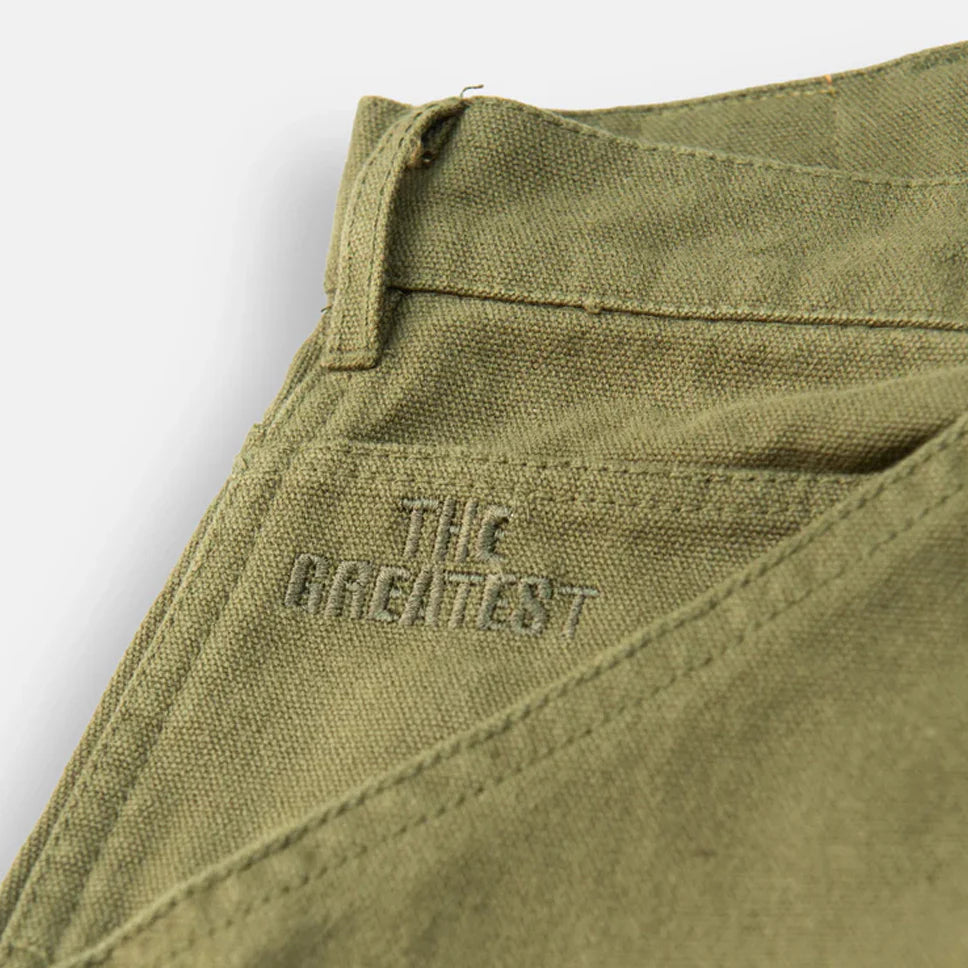 Close-up of green fabric with 'The Greatest' embroidered on it against a light gray background