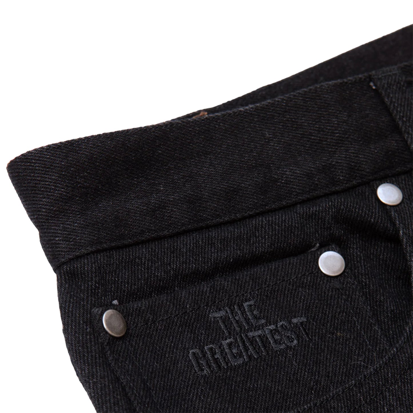 Close-up of black pants with 'The Greatest' text and buttons on a white background