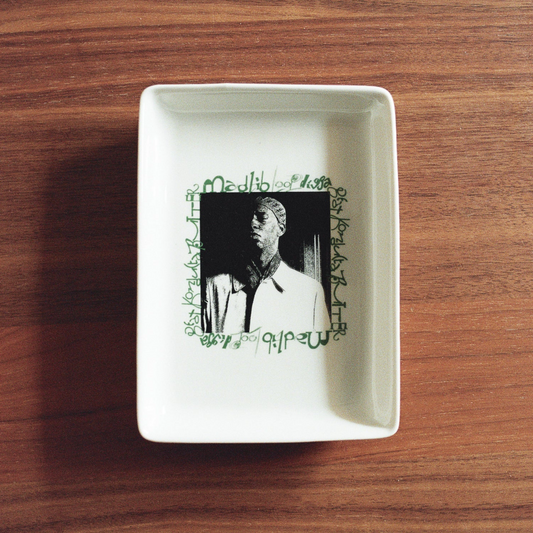 White square dish with a black and white portrait and green text on a wooden surface