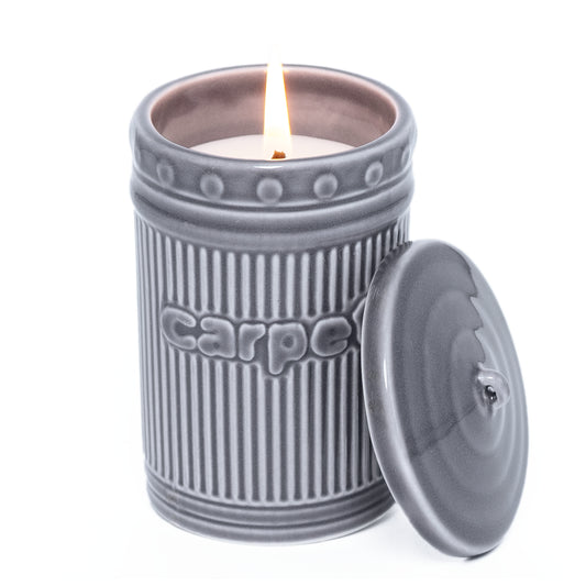 Gray ceramic candle jar with a lit candle inside on a white background