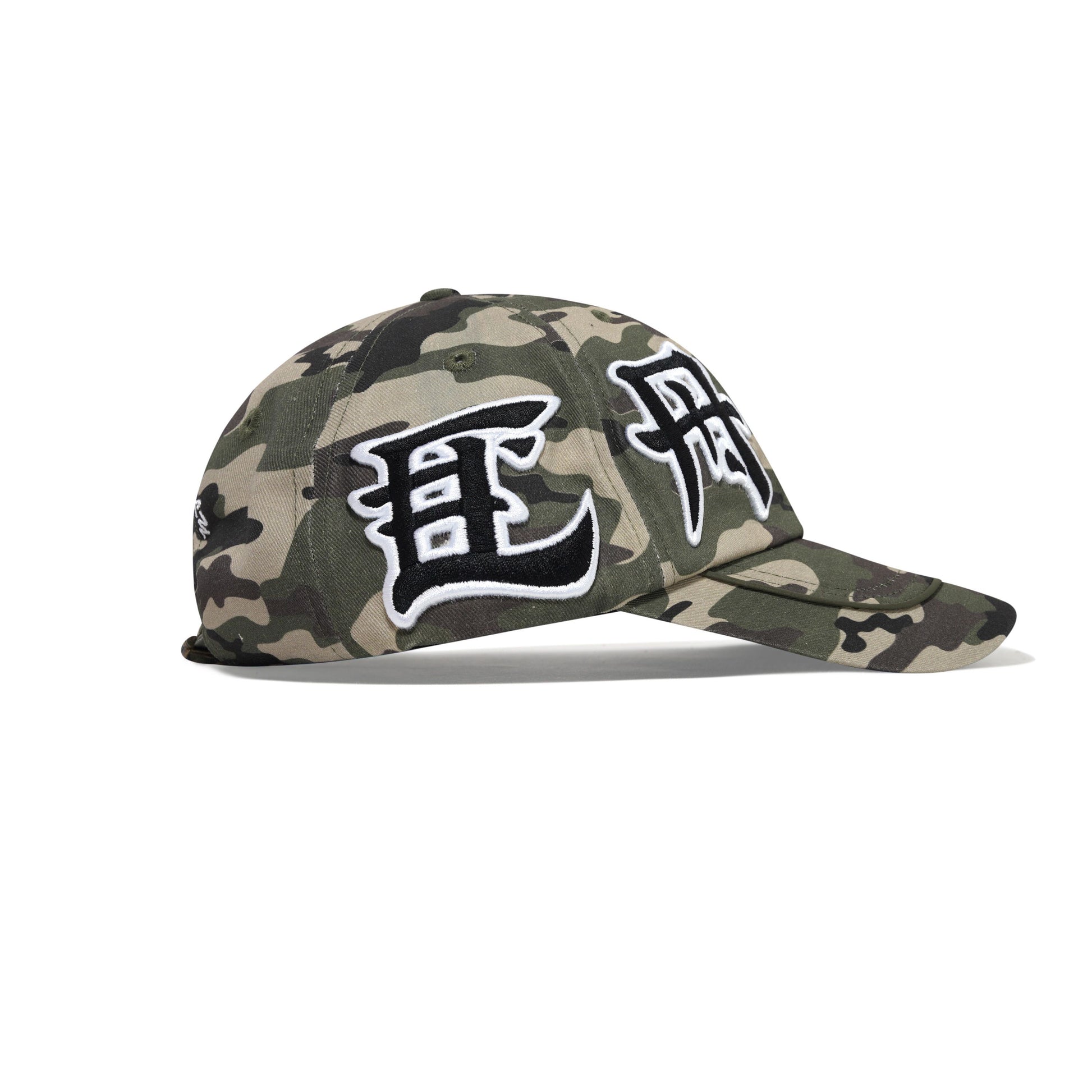 A baseball cap in a green and brown camouflage pattern, featuring large black and white embroidered Korean characters on the front panels, set against a plain white background.