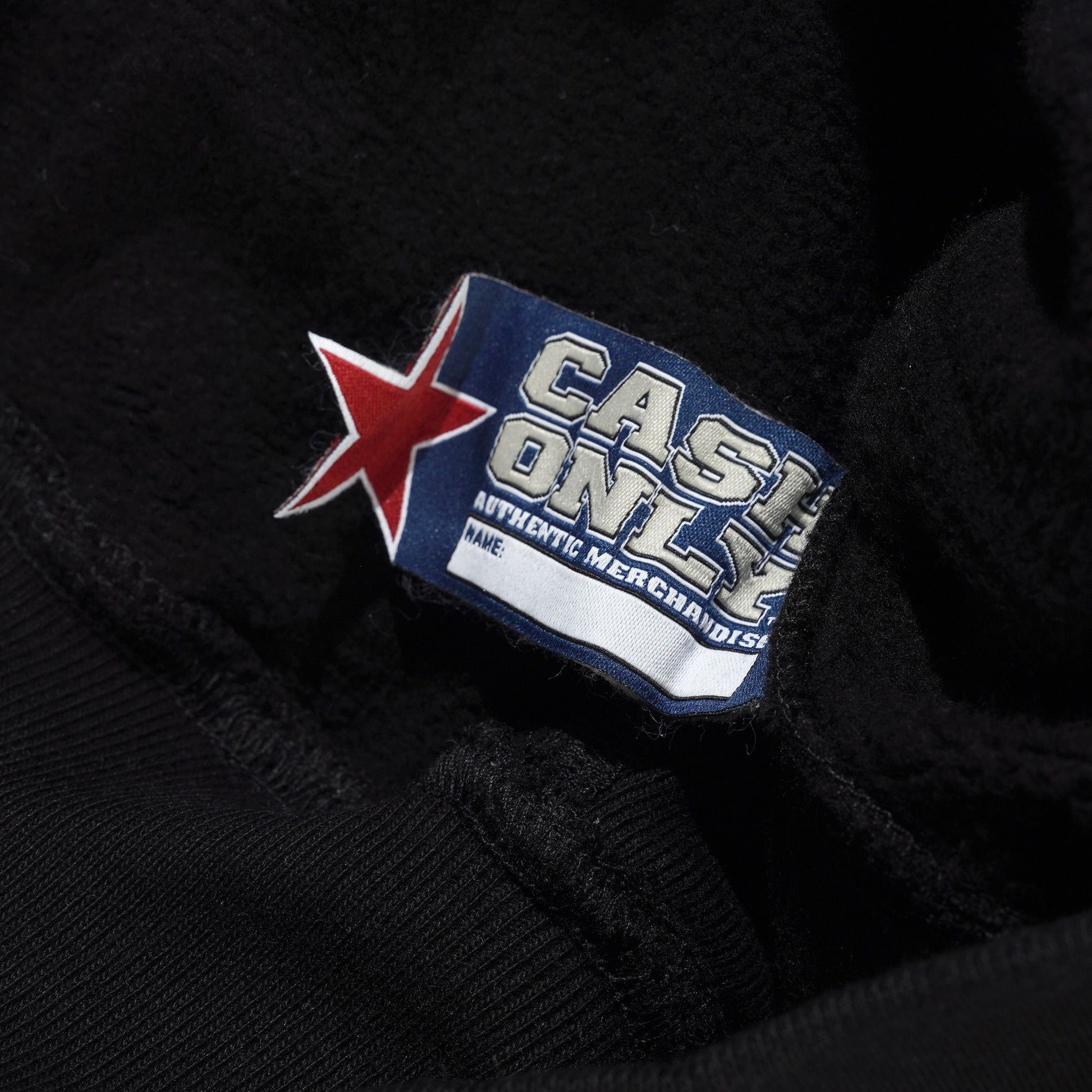 Close-up of a black jacket with a 'Cash Only' brand label featuring a red star.