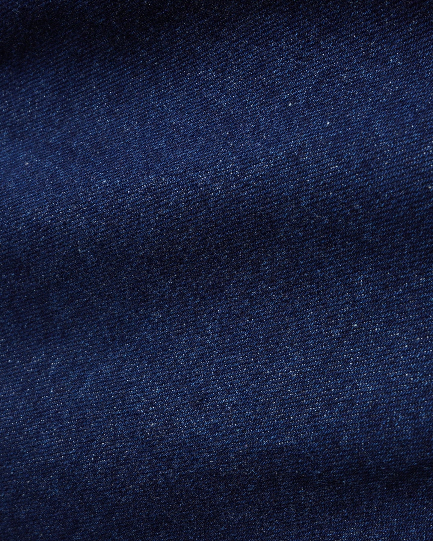 A close-up of dark navy blue denim fabric texture with subtle woven grain and slight shading.