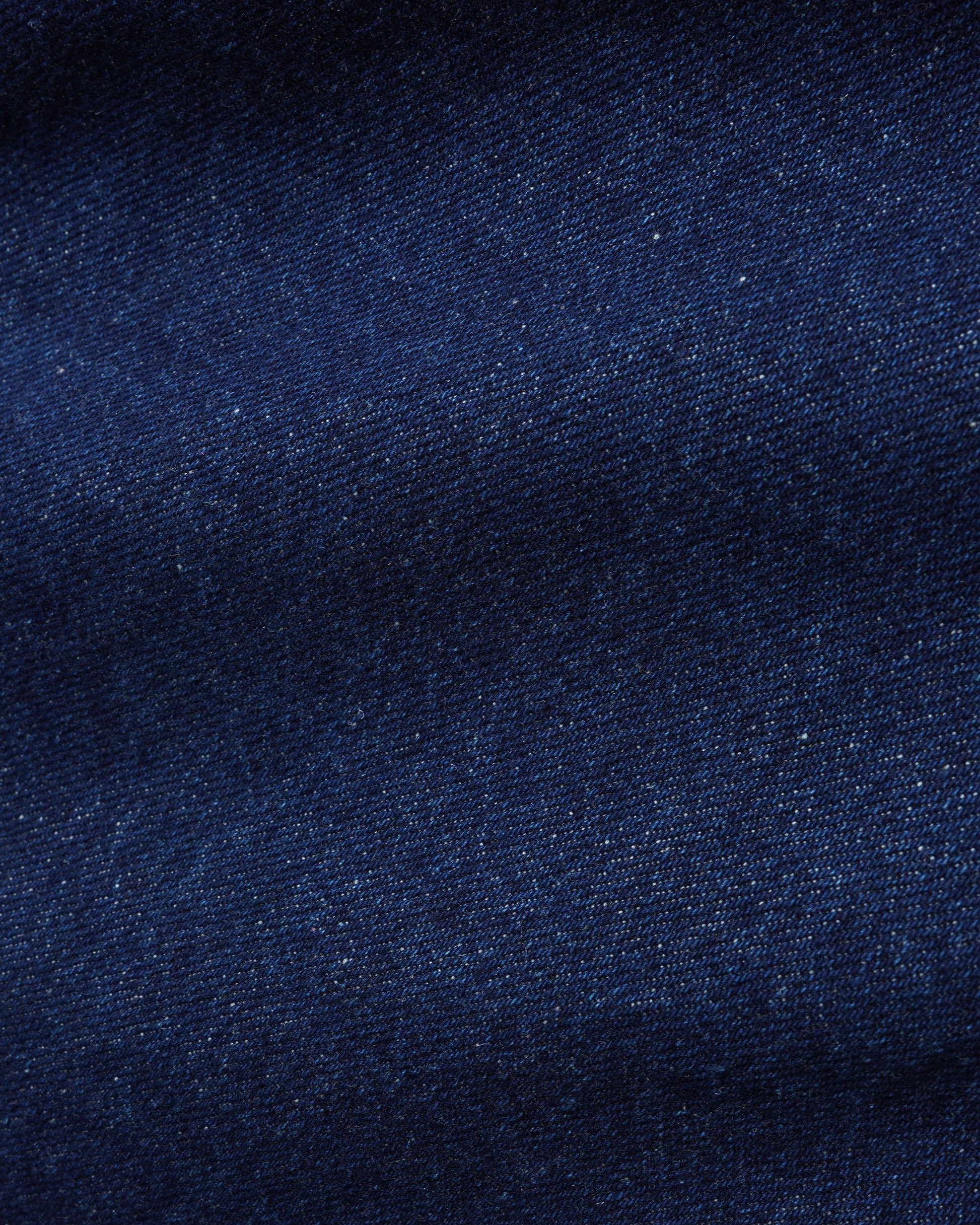 A close-up of dark navy blue denim fabric texture with subtle woven grain and slight shading.
