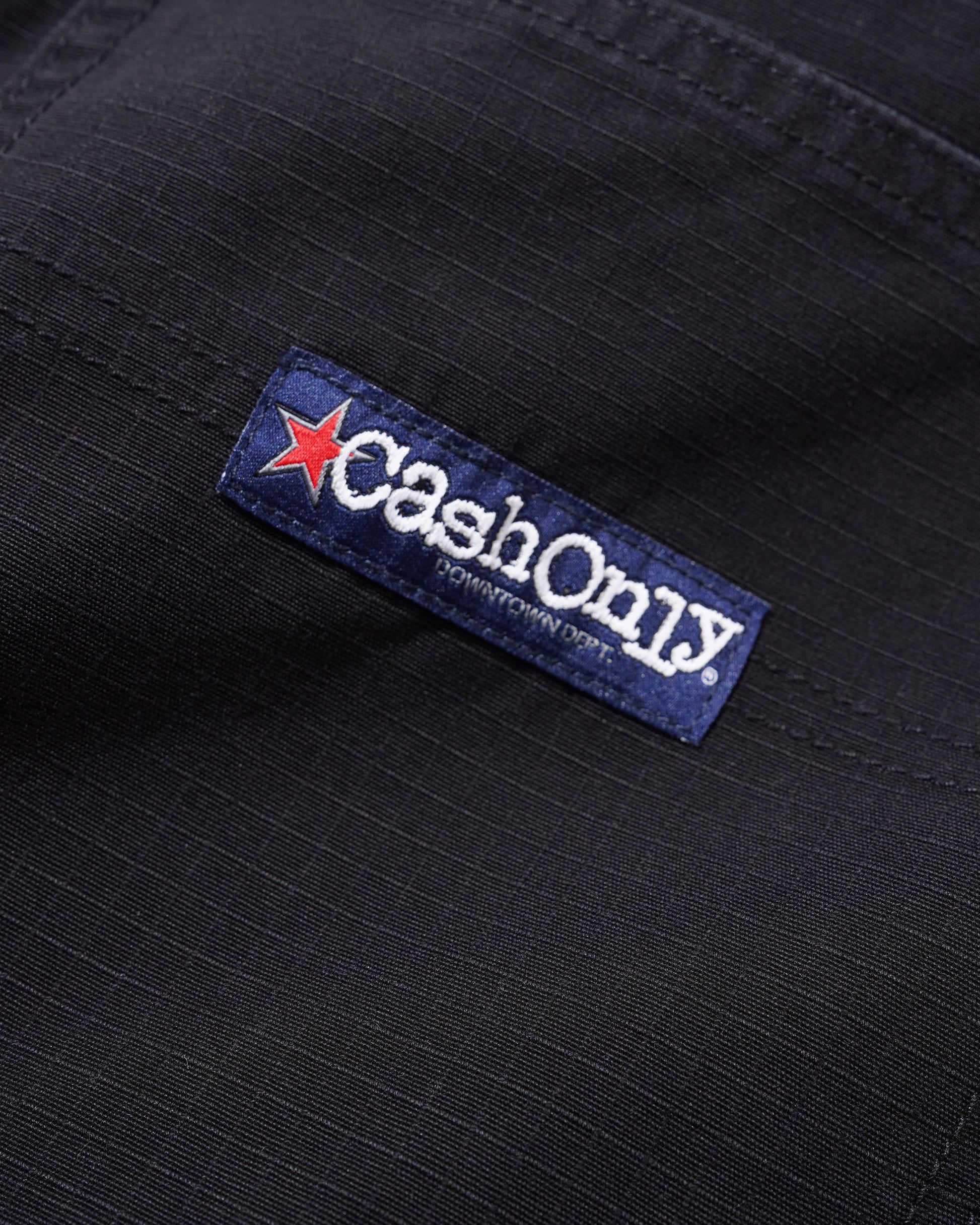Close-up of a black ribbed fabric garment featuring a blue woven brand label that reads 'Cash Only' with a red star and smaller text 'Downtown Sports'.