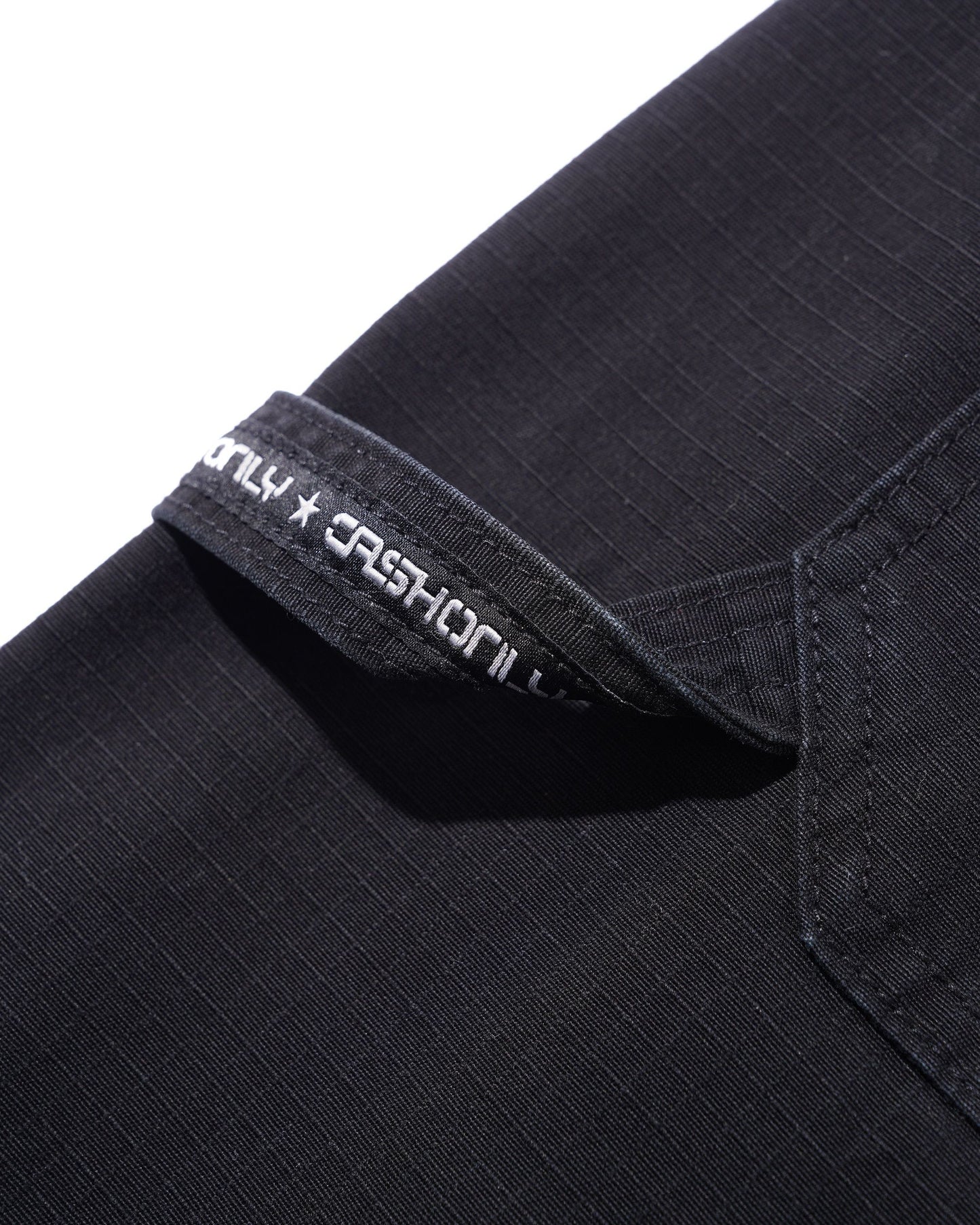 Close-up of a black ribbed fabric garment, likely a shirt or jacket, showing a folded collar with white embroidered text reading 'ONLY x FASHION'.