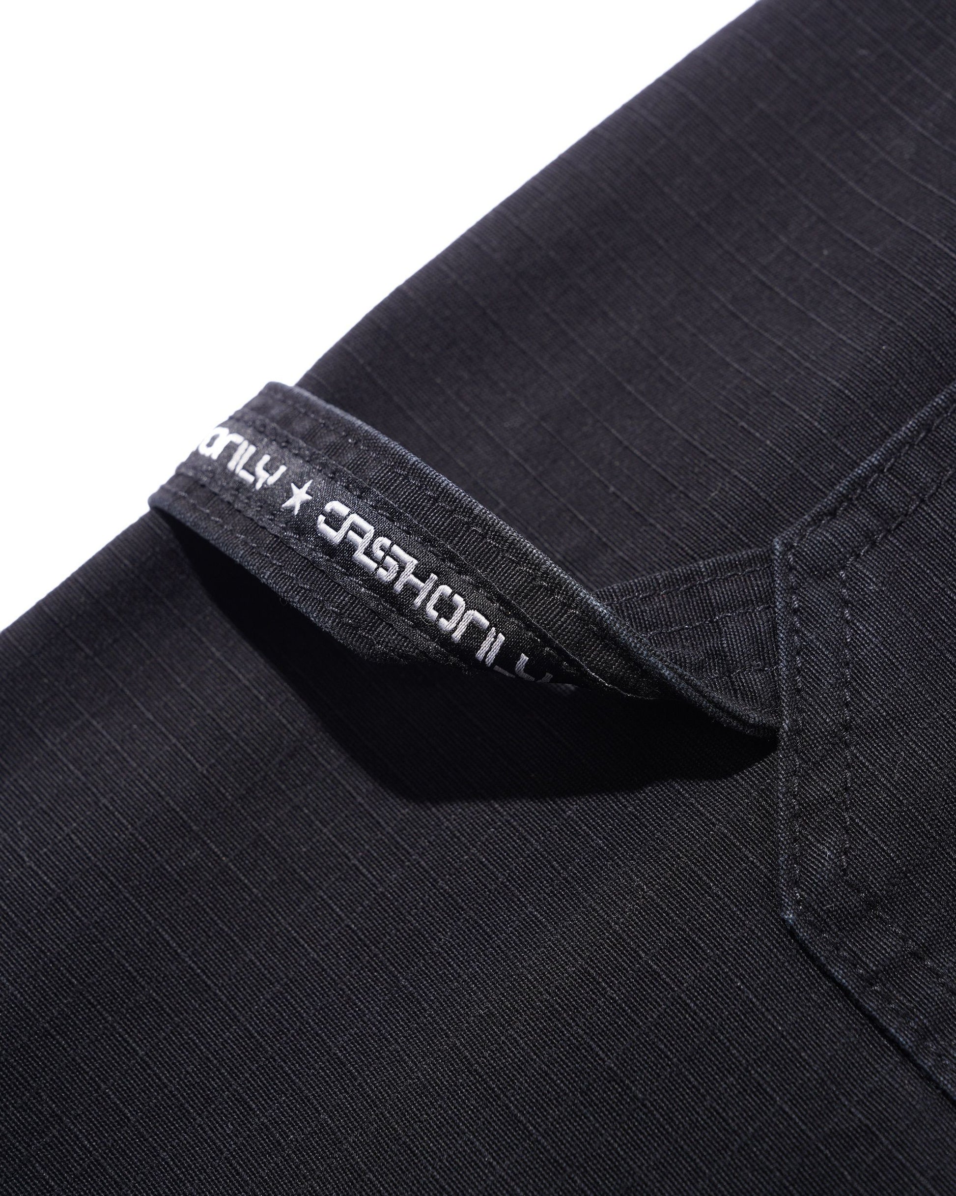 Close-up of a black ribbed fabric garment, likely a shirt or jacket, showing a folded collar with white embroidered text reading 'ONLY x FASHION'.