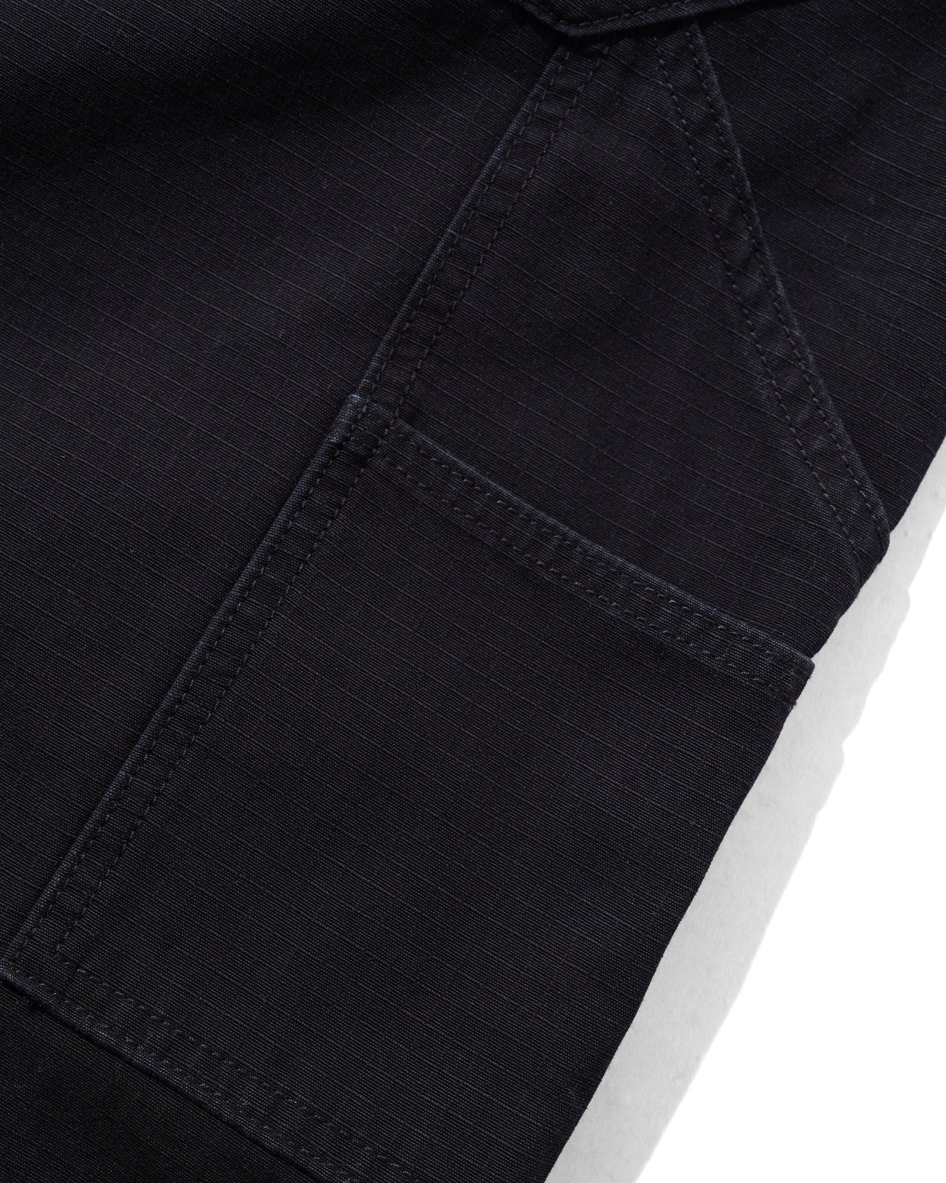 Close-up detail of a black denim garment showing a pocket seam and fabric texture against a white background.
