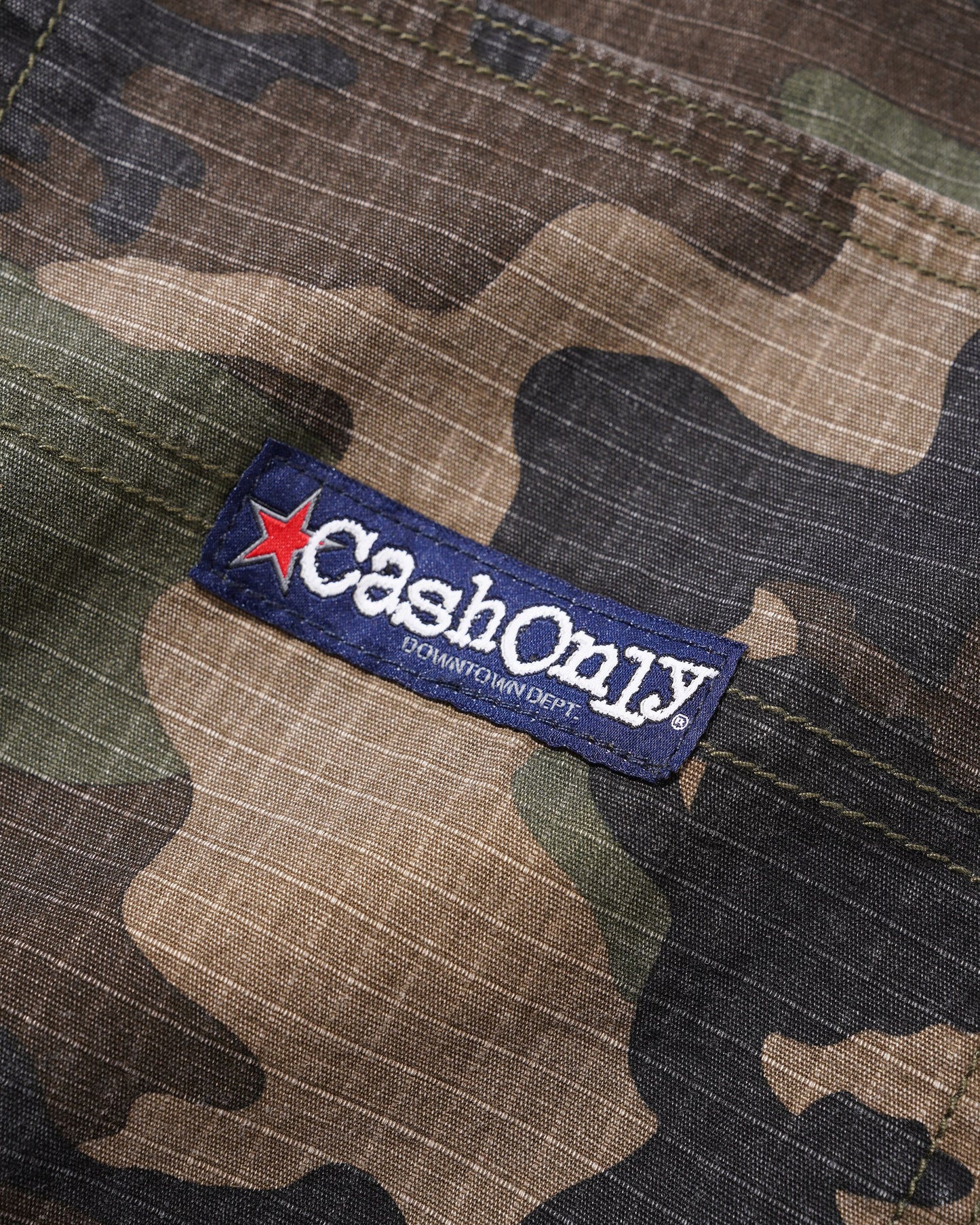 Close-up of a camouflage-patterned garment with a visible CashOnly brand patch on the fabric.