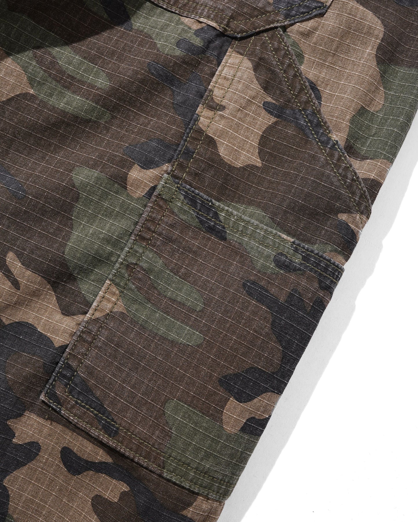 Close-up of camouflage cargo pants showing a brown, green, and tan camo pattern with a diagonal grid texture, featuring a side cargo pocket and a button closure.
