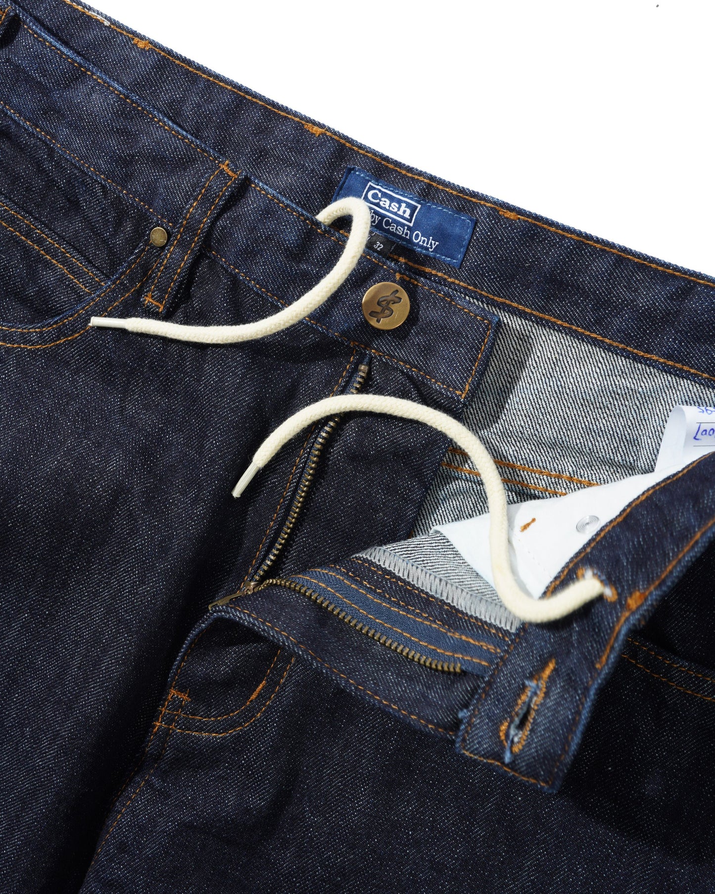 Close-up of dark indigo denim jeans showing the waistband, button closure, white drawstring, zipper pocket, and interior lining. A blue waistband label reads Chaps.