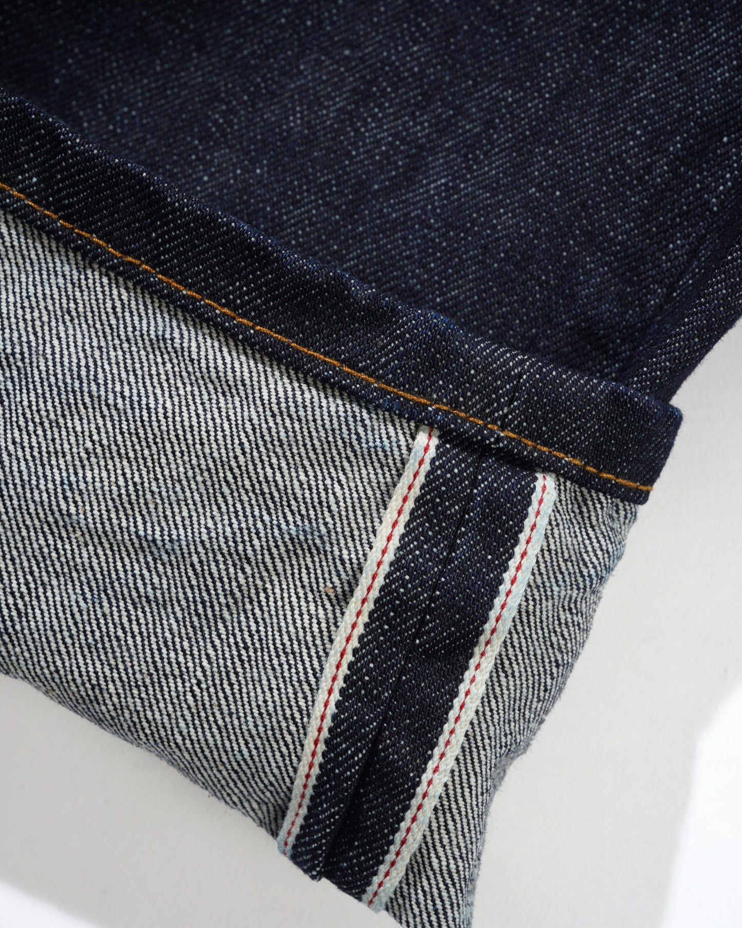 Close-up of a rolled-up pair of dark indigo denim jeans showing the dark blue outer fabric and the lighter gray inner lining with contrast orange and white stitching.