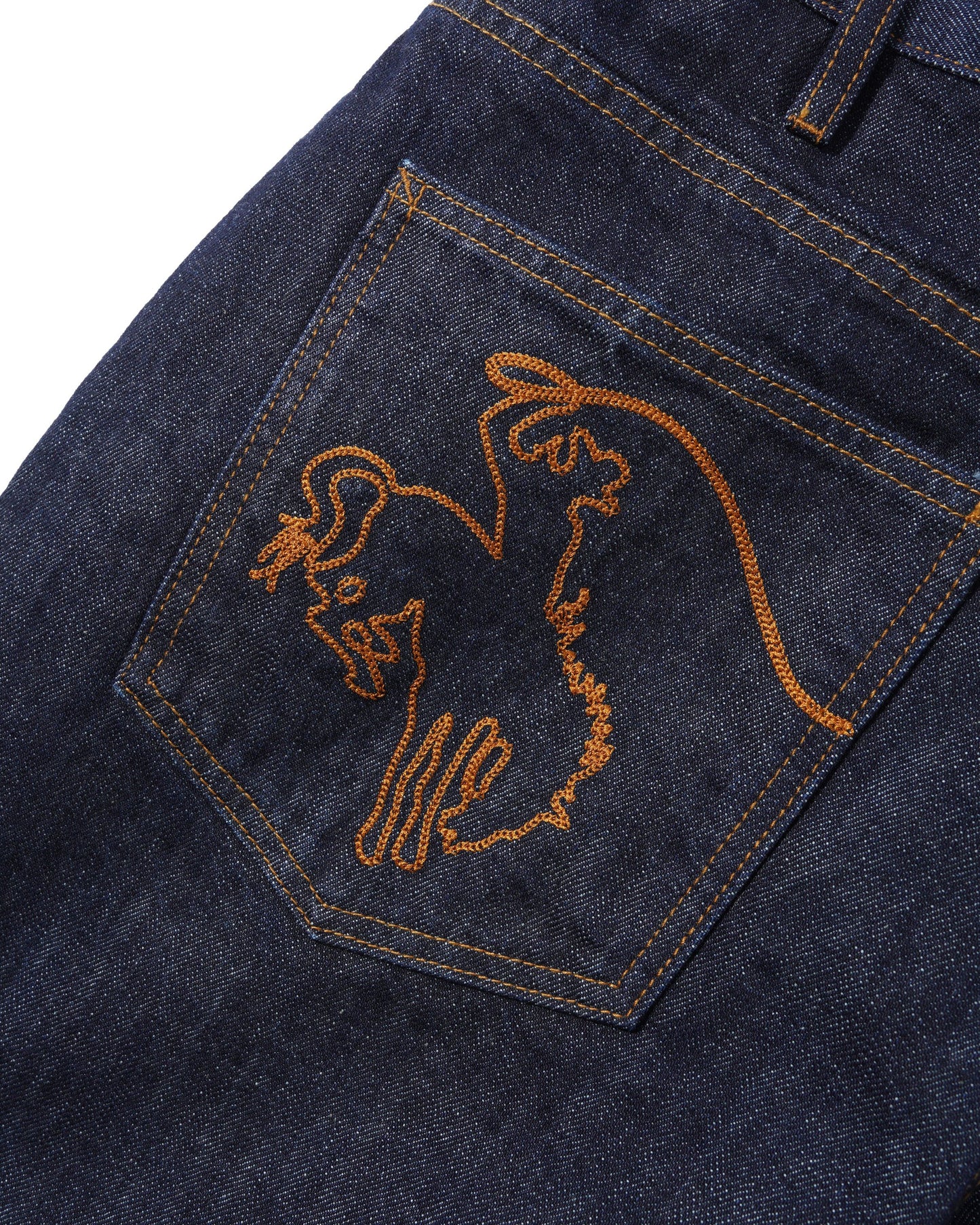 Close-up of a dark indigo denim pocket with orange embroidery of a cowboy profile and a small circular logo.