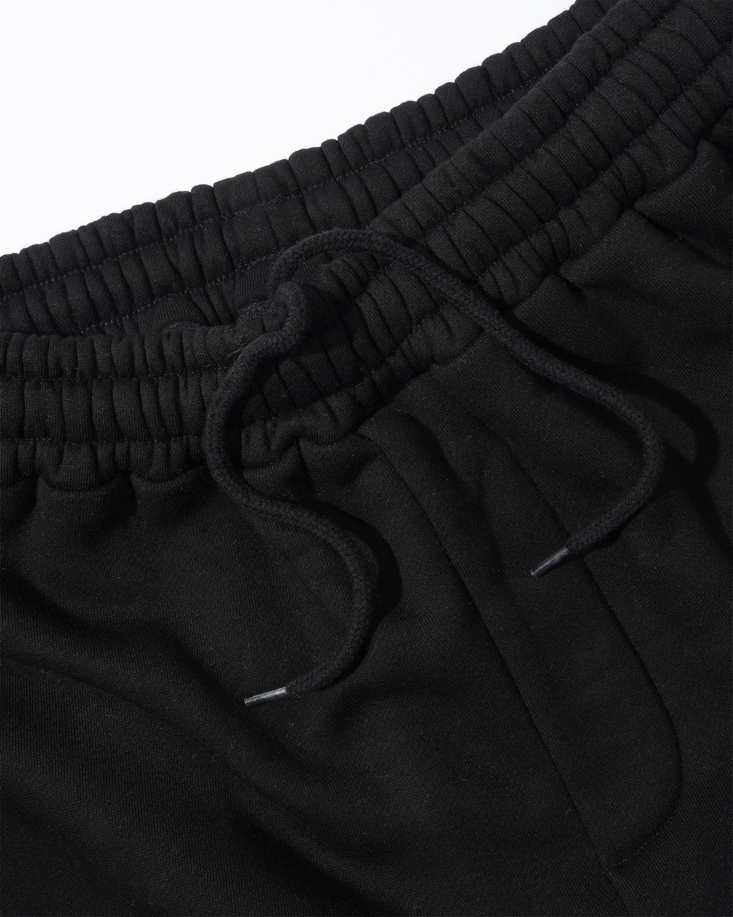 Close-up of black drawstring sweatpants showing the ribbed elastic waistband and black drawstring cords against a white background.