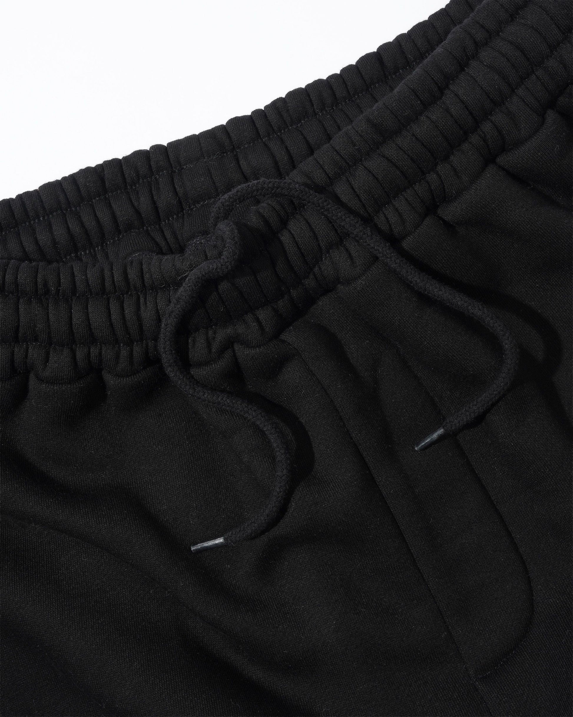 Close-up of black drawstring sweatpants showing the ribbed elastic waistband and black drawstring cords against a white background.