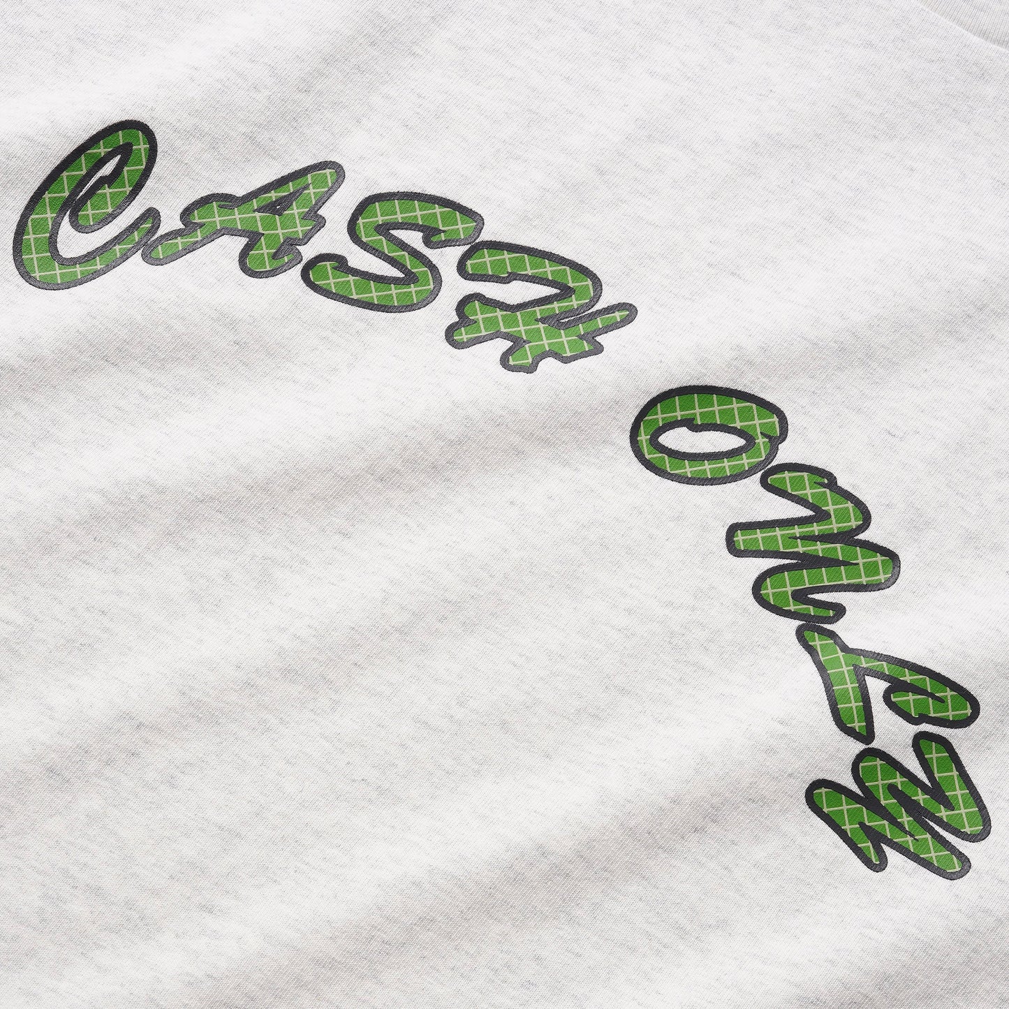 Close-up of a white heather t-shirt featuring a green plaid patterned script graphic that reads 'cash only' with a black outline.