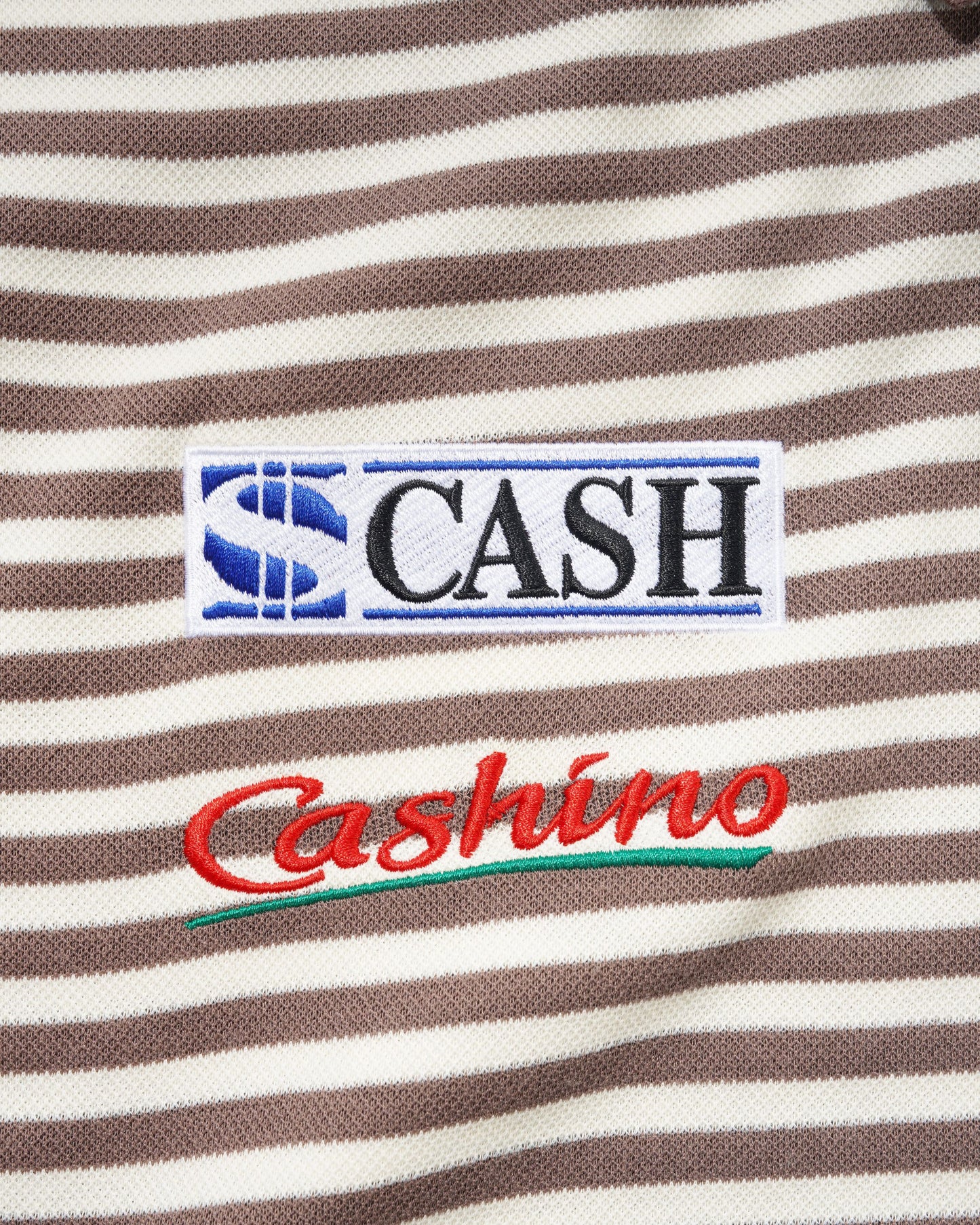 Close-up of a brown and cream striped fabric with embroidered patches. The top patch reads 'S CASH' in black letters with a blue 'S' logo, and the lower patch reads 'Cashino' in red script with a green underline.