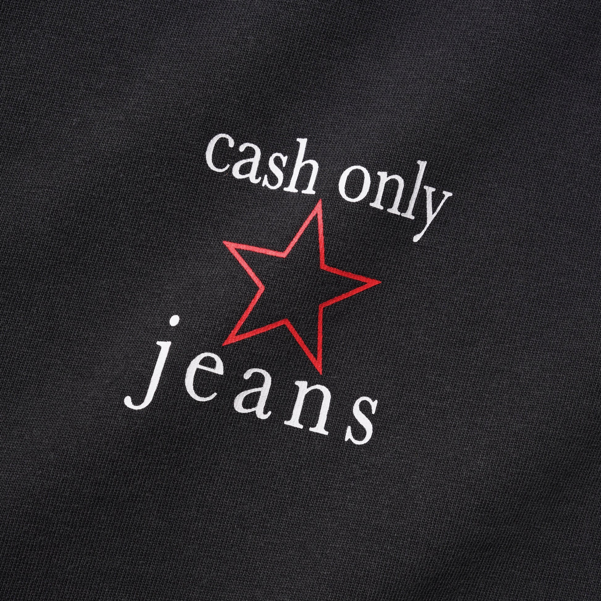 Close-up of a black fabric surface with white text reading 'cash only jeans' and a red outlined star graphic between the words.