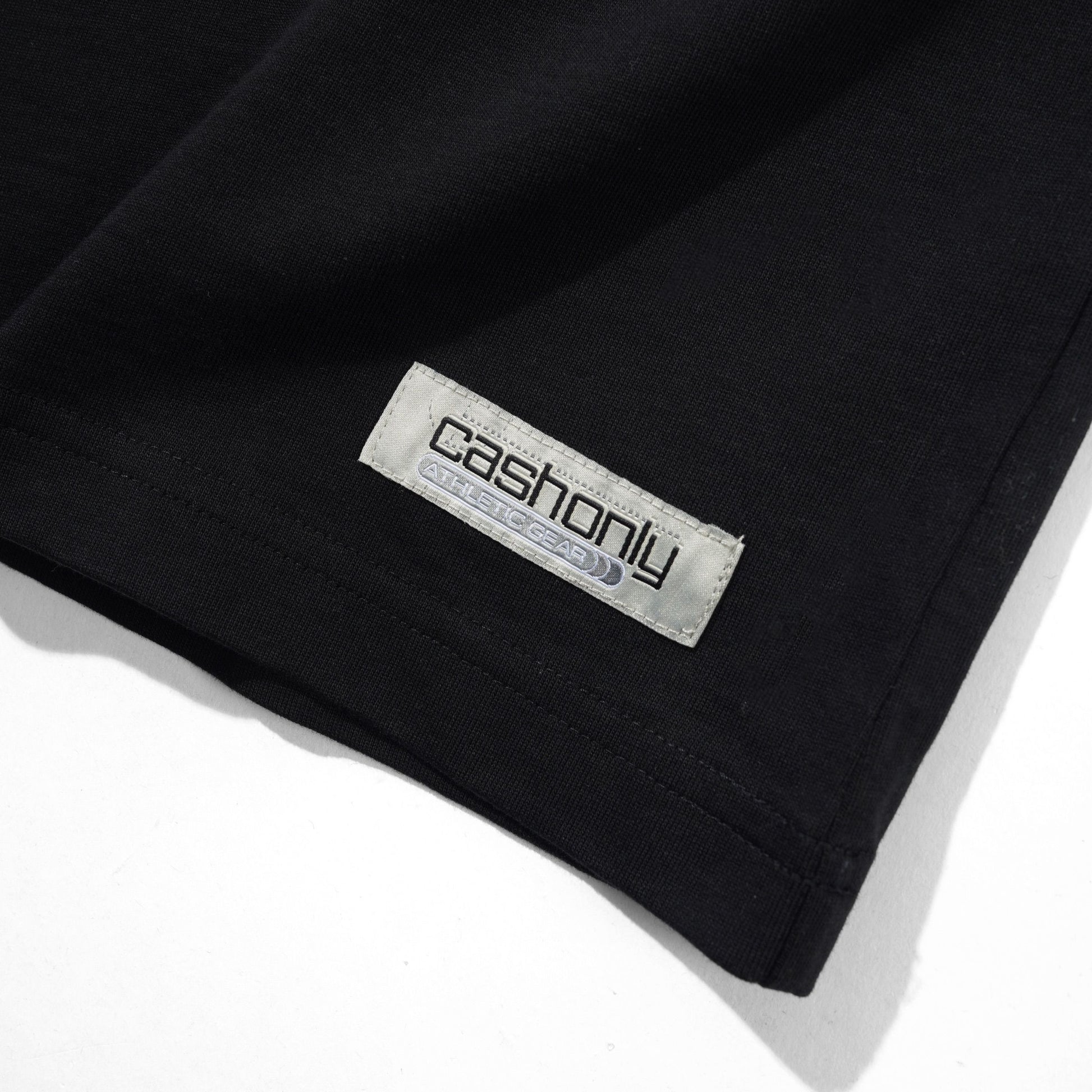 Close-up of a black garment corner with a visible rectangular brand label reading 'cashonly' on a white background.