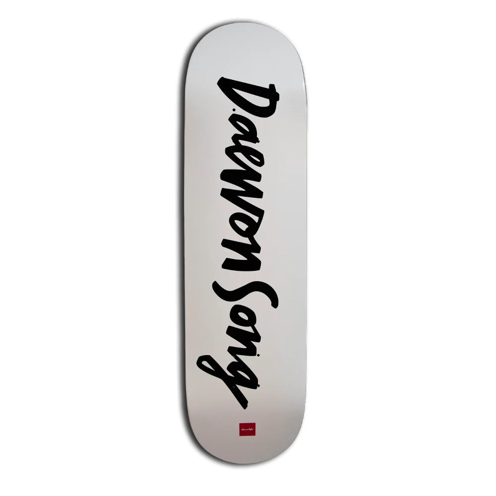 A skateboard deck with a white to light gray gradient background, featuring the brand name 'daewon Song' printed vertically in black script and a small red logo at the bottom.