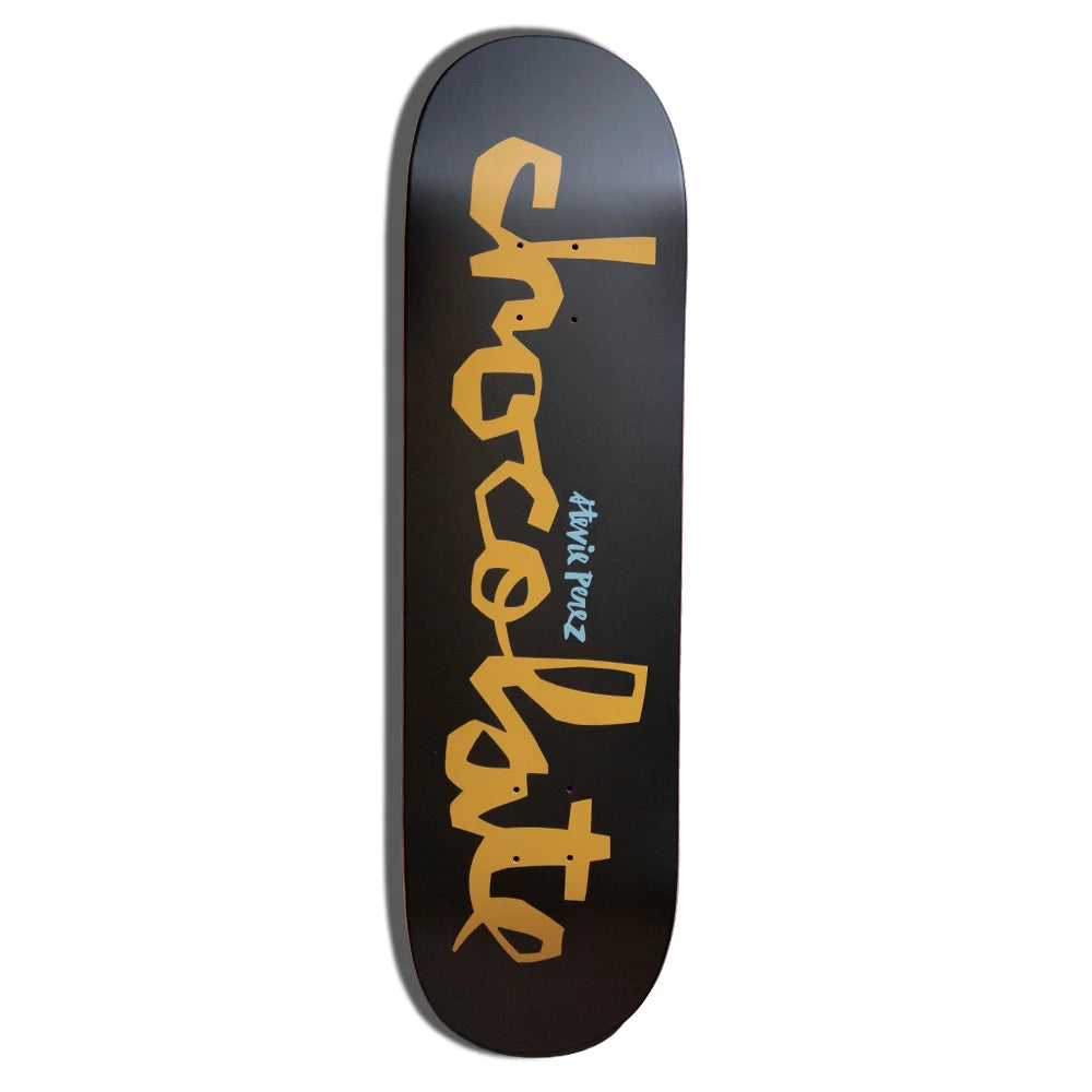 A skateboard deck with a black background and a large gold 'chocolate' graphic printed vertically, featuring 'stevie perez' in smaller text.
