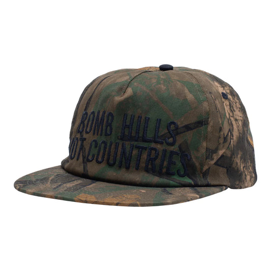 Camouflage cap with 'Bom Hills Hot Countries' text on a white background