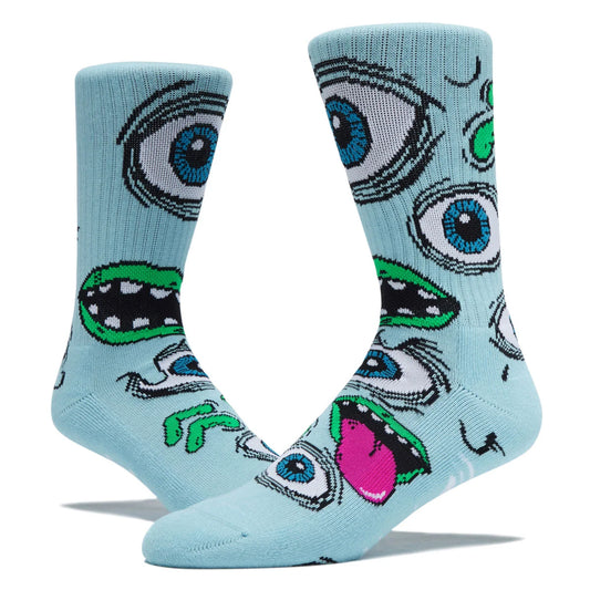 A pair of light blue crew socks featuring a bold, graphic cartoon monster face pattern with blue eyes, green teeth, and a pink tongue, displayed on a clean white background.