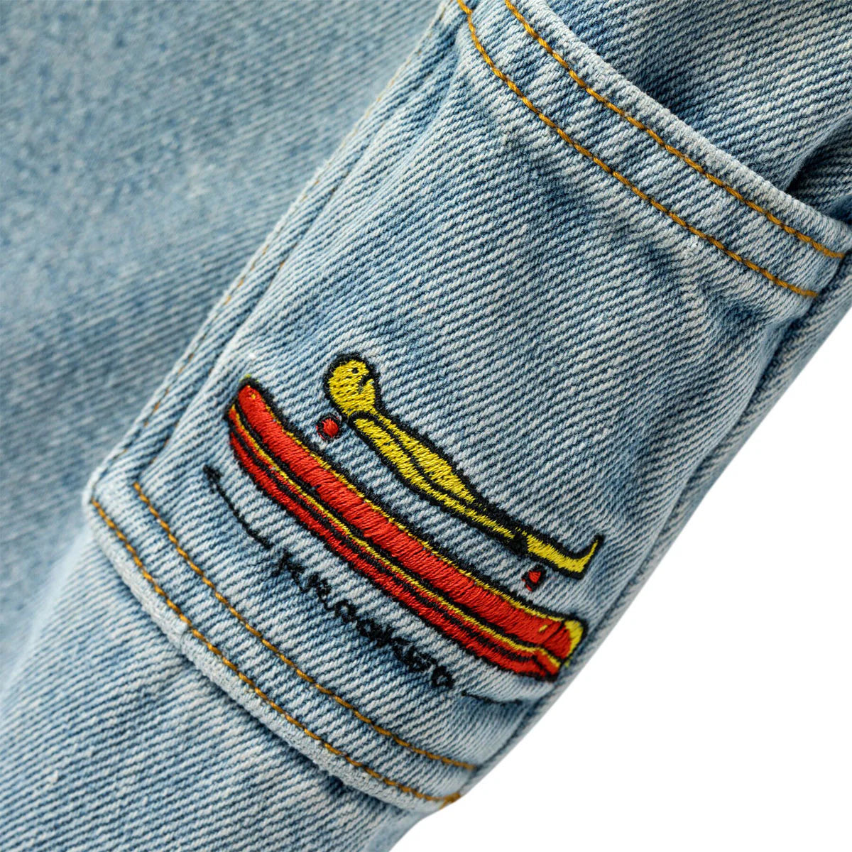 Embroidered design on a denim fabric with a red object and yellow figure.