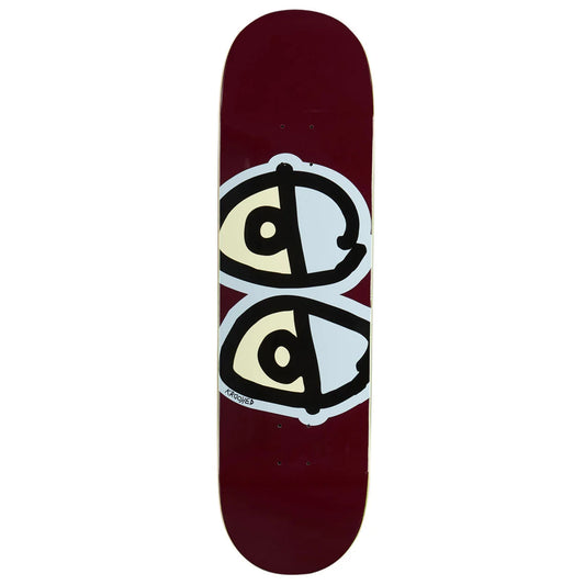 A skateboard deck with a deep burgundy background, featuring a large graphic of two stylized eyes in cream, black, and white on the underside.