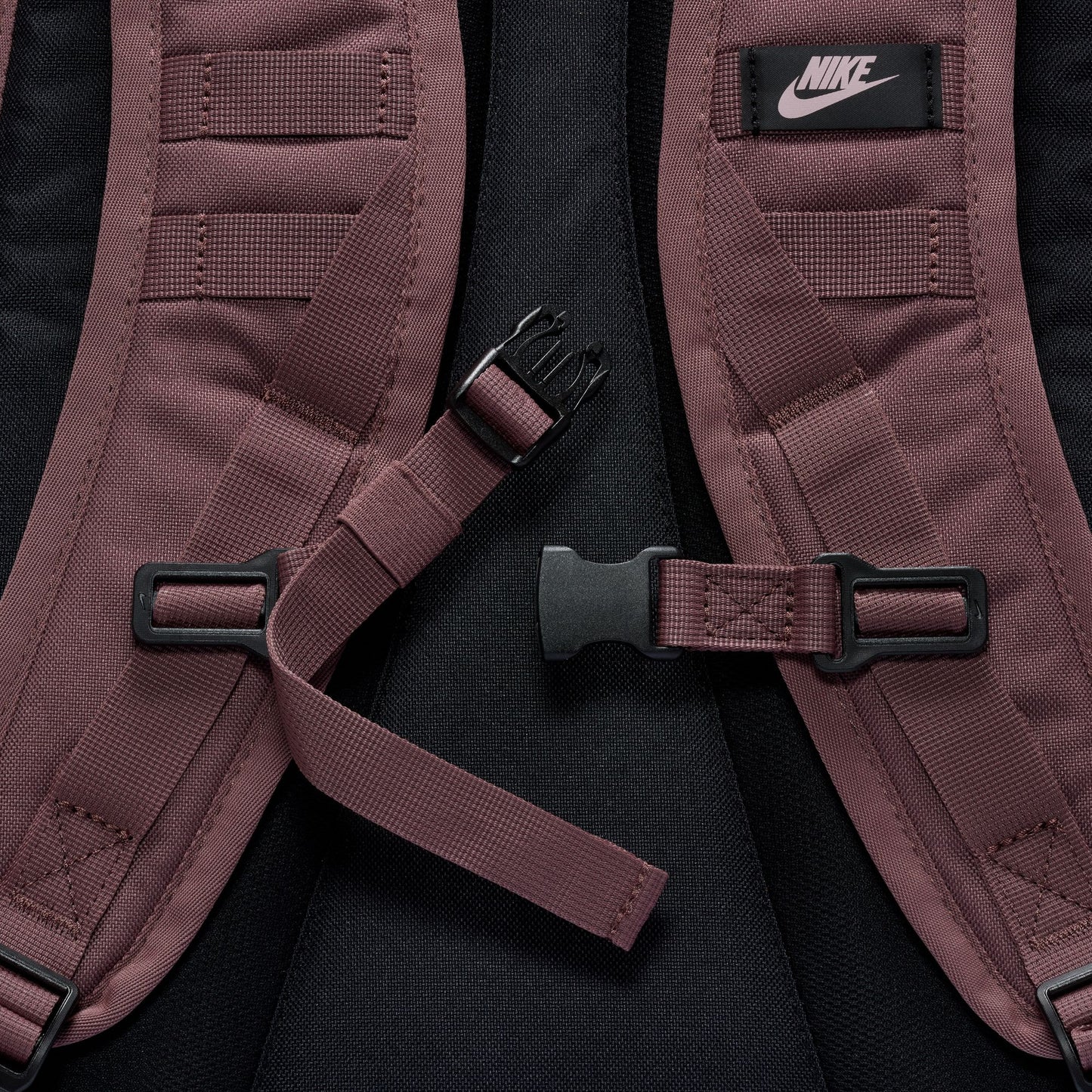 Close-up of a maroon backpack with black straps and Nike logo on a black background