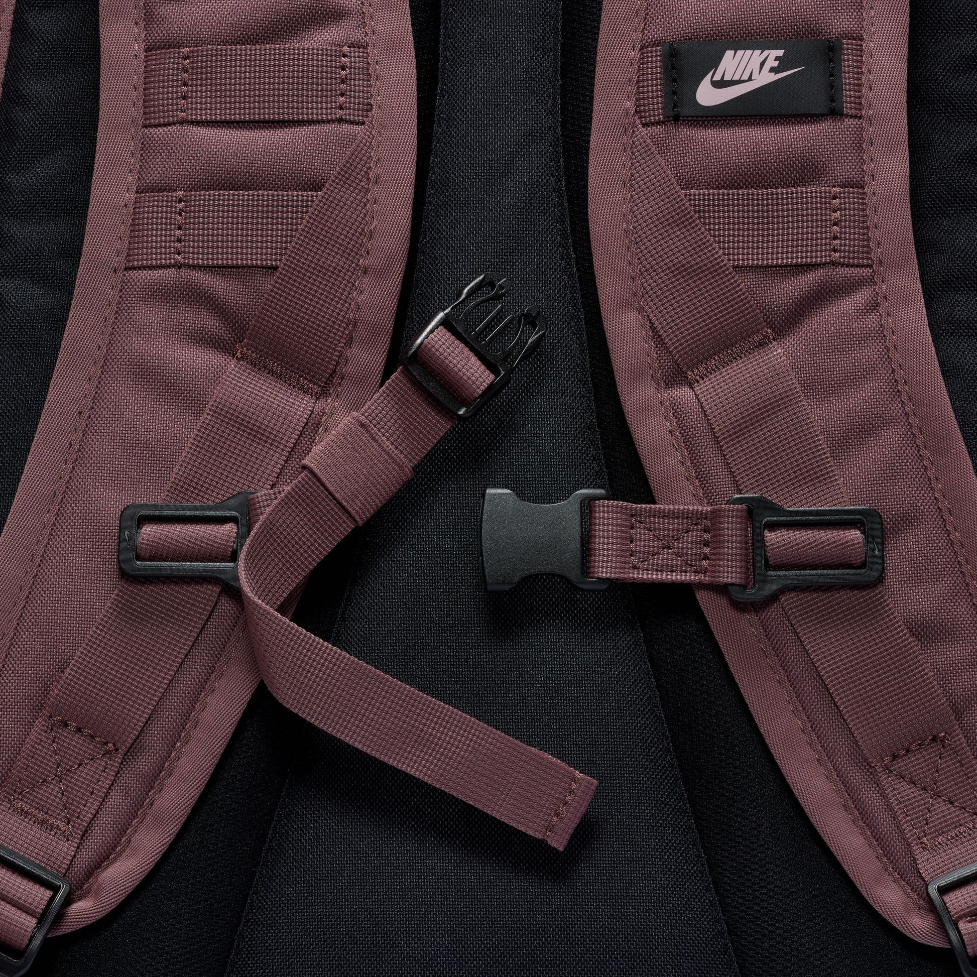 Close-up of a maroon backpack with black straps and Nike logo on a black background
