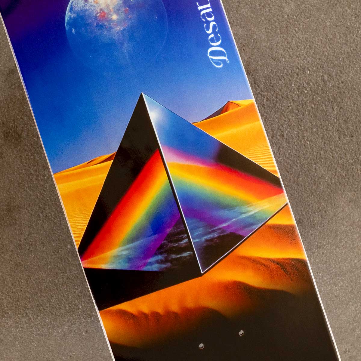 Desert-themed skateboard deck with pyramid and rainbow design on a textured surface