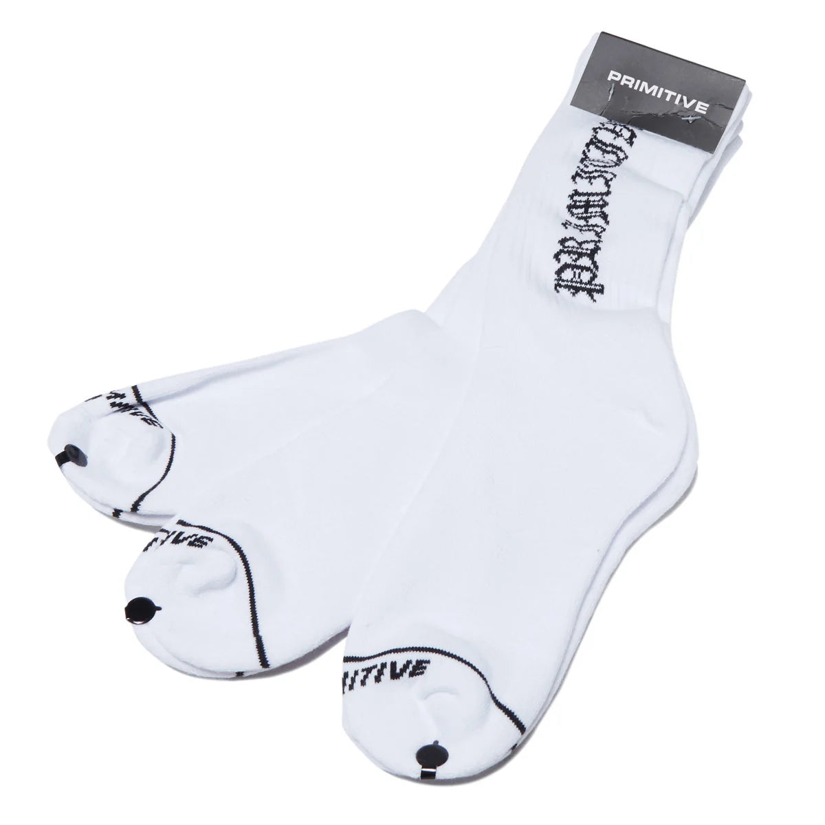 A pair of white Primitive crew socks with black gothic-style branding on the cuff and toe, shown on a clean white background with the brand's retail tag still attached.