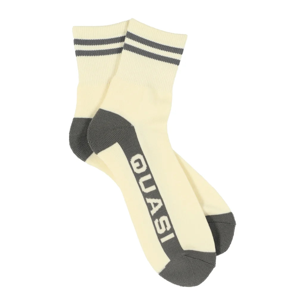 A pair of cream-colored crew socks with dark gray accents, featuring double stripes on the cuff, a dark gray heel and toe, and the brand name 'QUASI' printed vertically on the side.