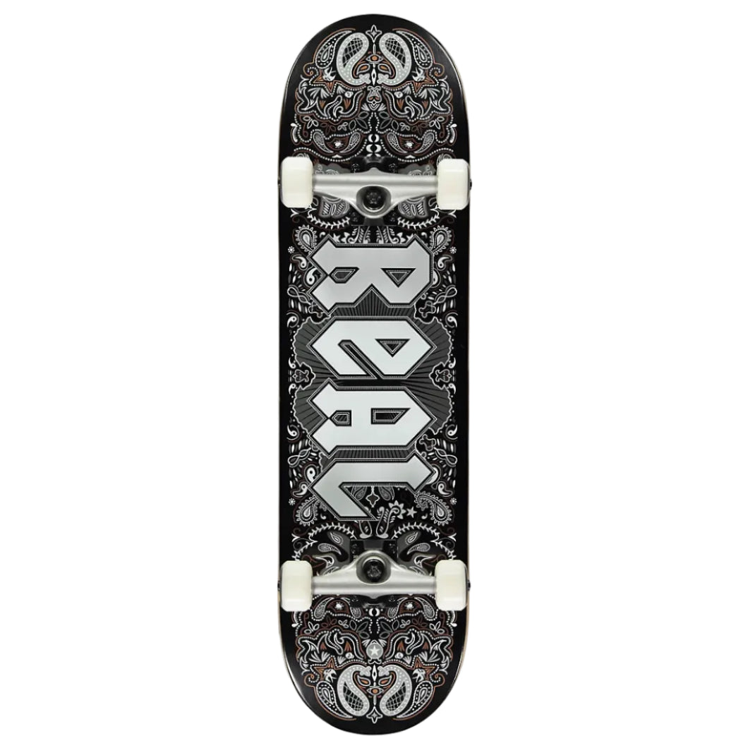 A skateboard deck shown vertically against a light gray background, featuring a black base with intricate silver and white paisley-style graphics and the word 'REAL' printed vertically in large silver letters.