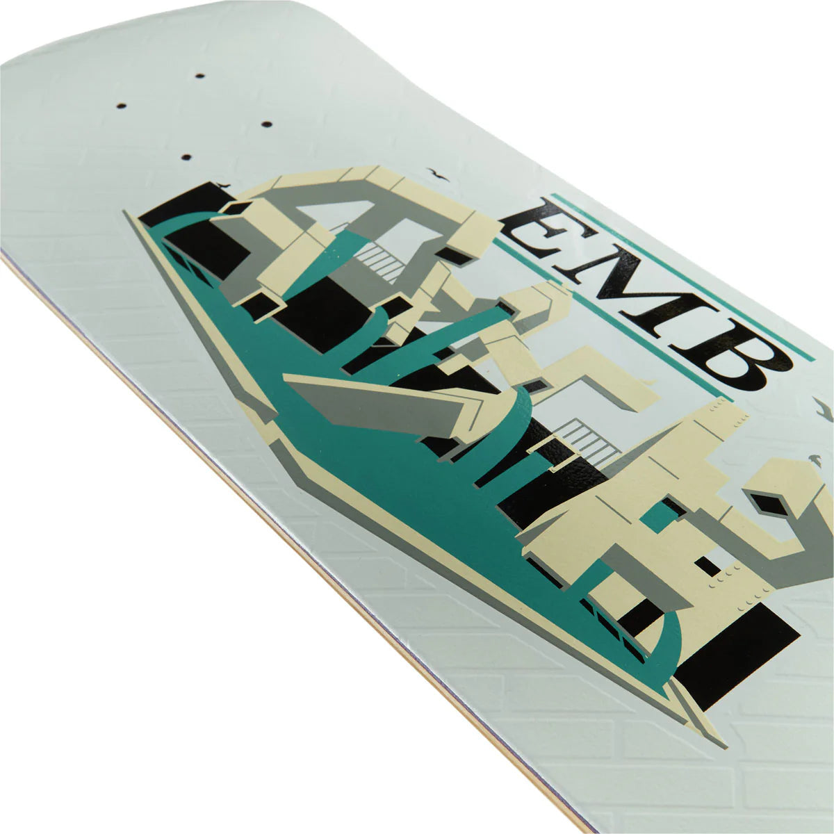A close-up of a skateboard deck showing a large graphic design with the text 'EMB' and a stylized building illustration in teal, beige, black, and gray on a white deck.