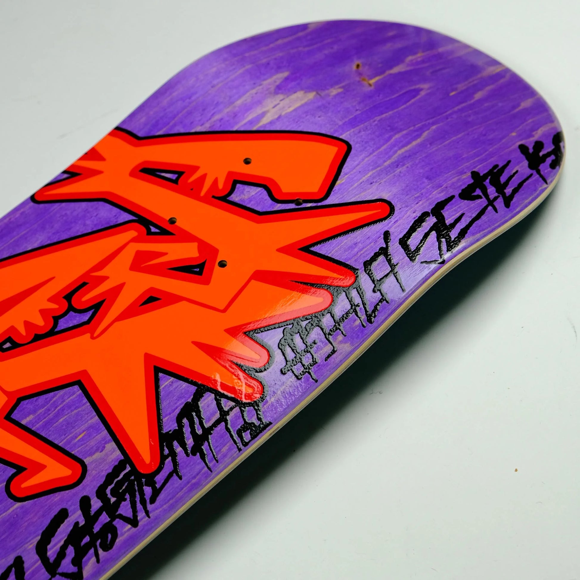 Skateboard deck with orange logo and purple background on a white surface